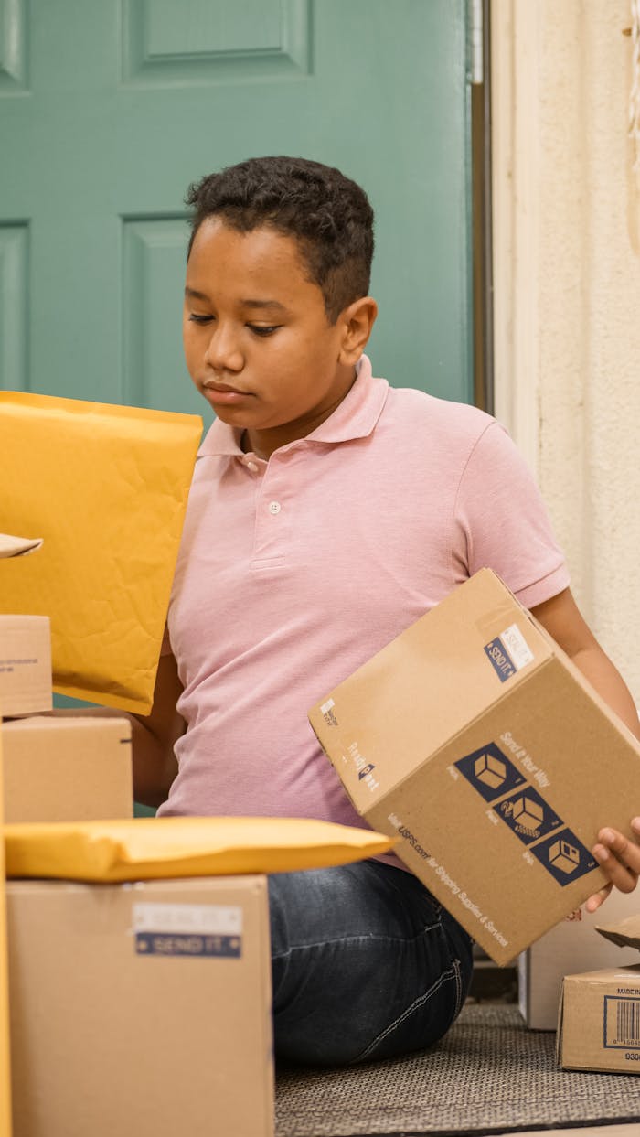 A young boy sits on a porch organizing large and small delivery packages.